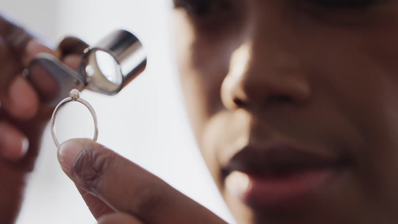 African american female worker inspecting ring with magnifying glass in workshop in slow motion
