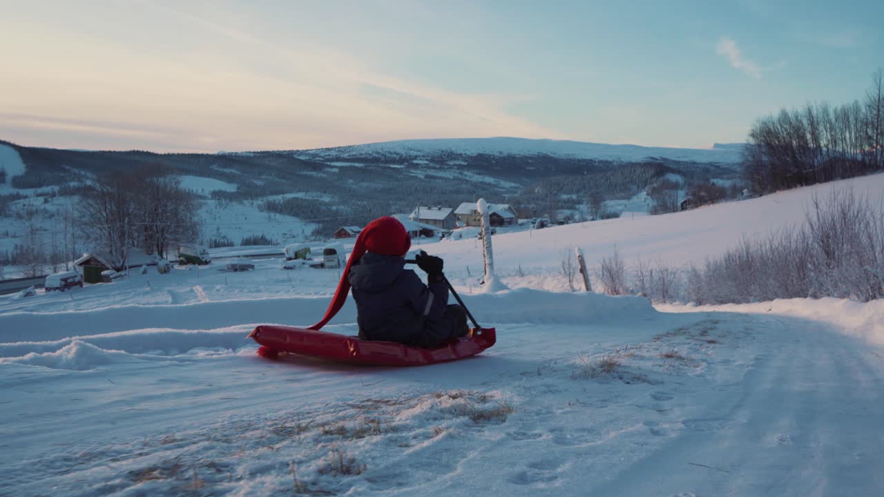 toma de seguimiento de un niño divirtiéndose en la nieve con trineo usando una pala roja de plástico en trineo