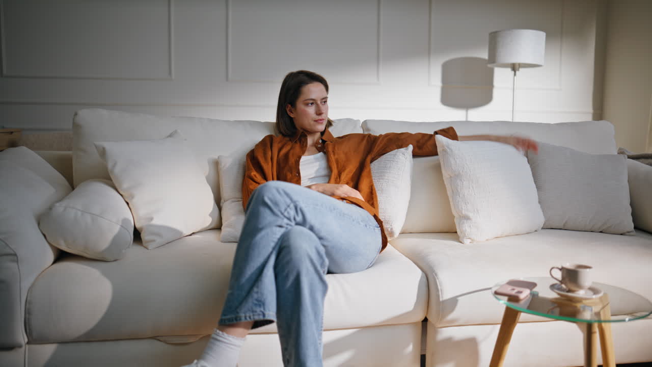 Home girl sitting couch enjoying comfortable interior. Brunette falling on sofa