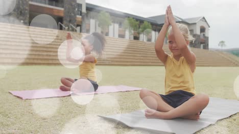 animation of light spots over happy diverse schoolgirls sitting in outdoor yoga class