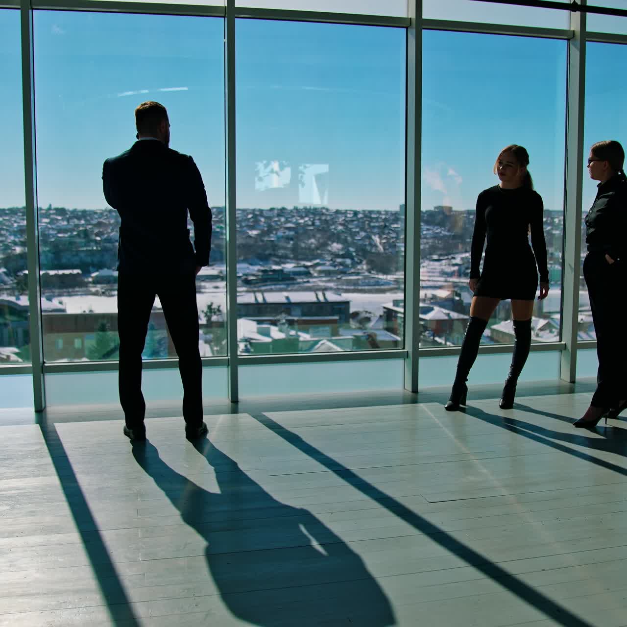 Young people indoors on large windows background. Beautiful business women talking about man. Businessman standing in office near windows in sunny day
