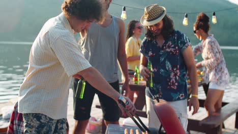 male friends grilling sausages and drinking beer on lake party