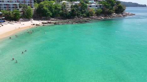 drone footage captures a vibrant phuket beach with turquoise waters, tourists, and lush greenery under bright daylight