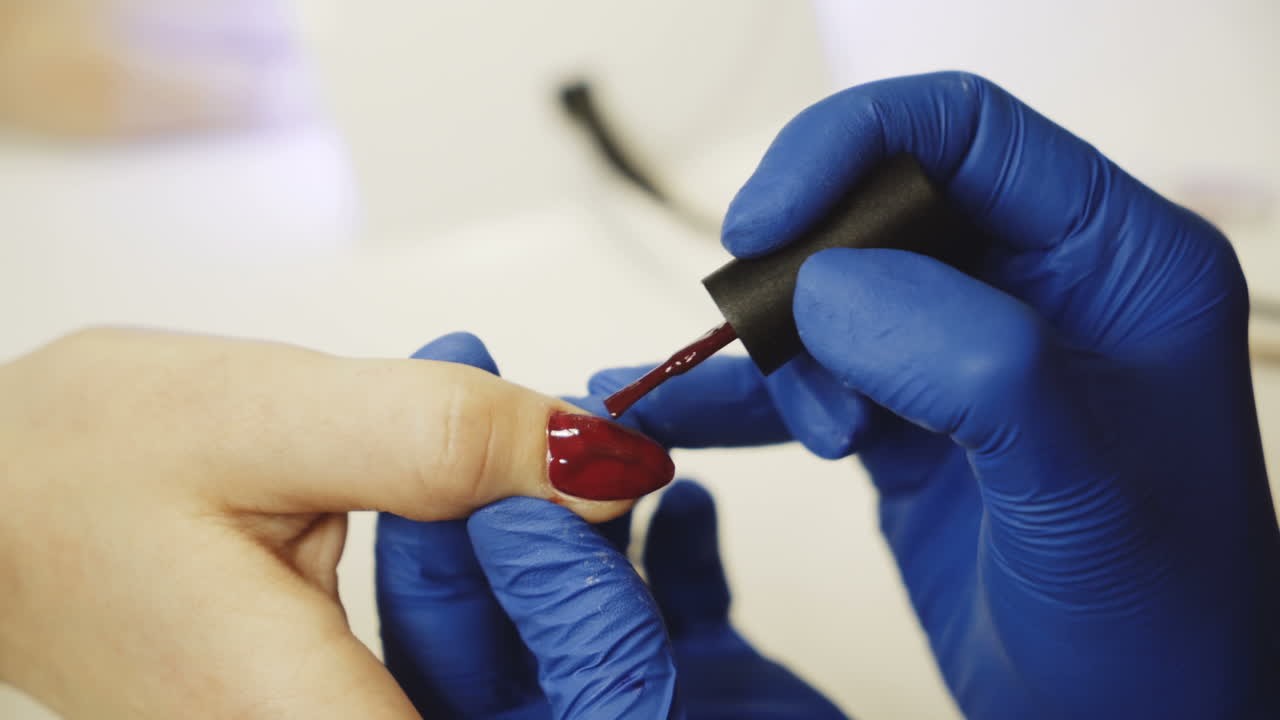 Master of nails paints nails with red lacquer in the salon. Relaxing day at beauty salon. Close-up