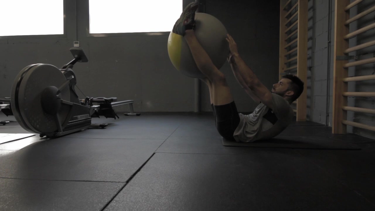 Giovane uomo atletico che allena gli addominali bassi con una palla da Pilates in palestra.