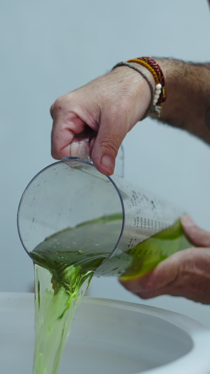 Primer plano de unas manos vertiendo un vibrante líquido verde desde un vaso medidor