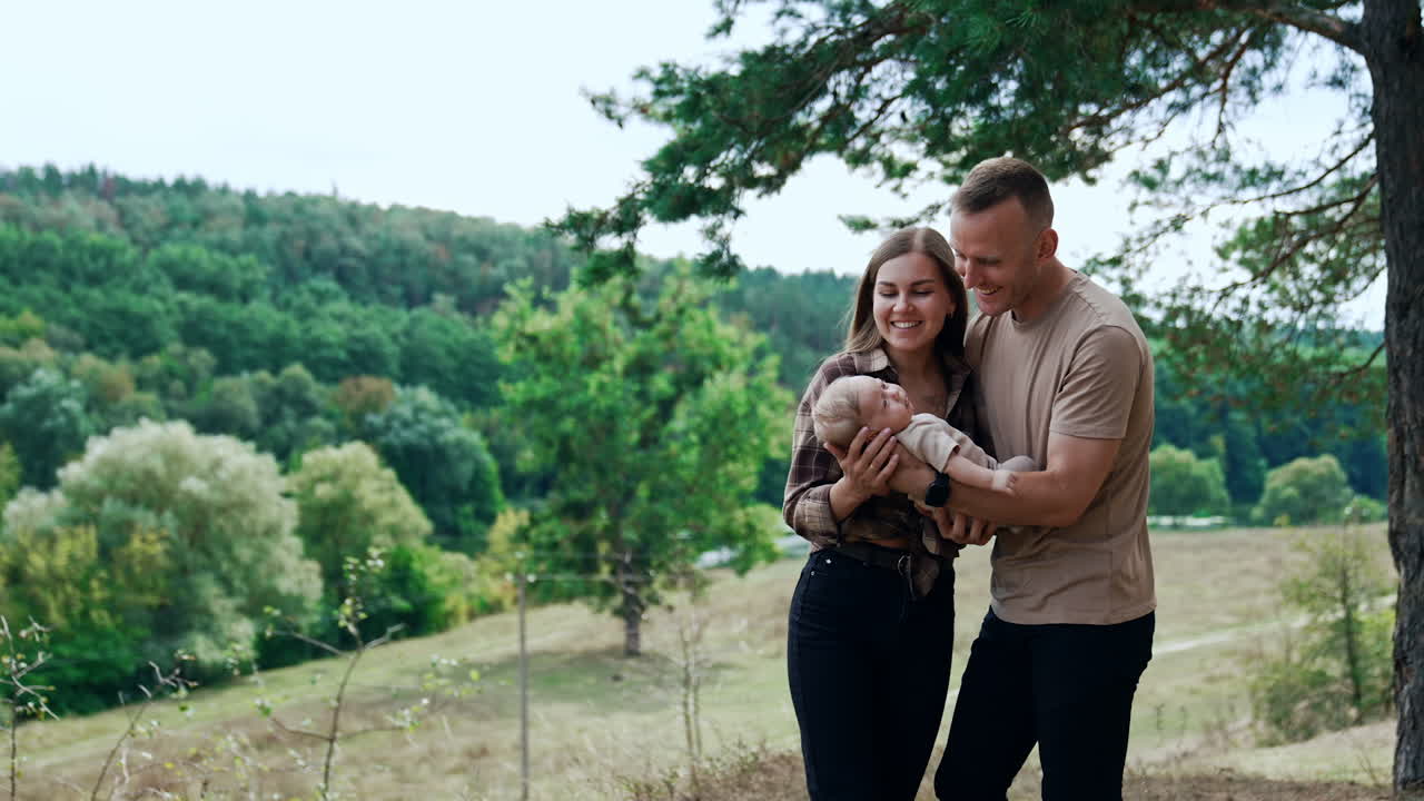 Smiling happy couple hold their baby boy talking to him. Parents of a newborn in nature.