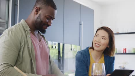 video of happy diverse couple preparing food using recipe on tablet in kitchen at home