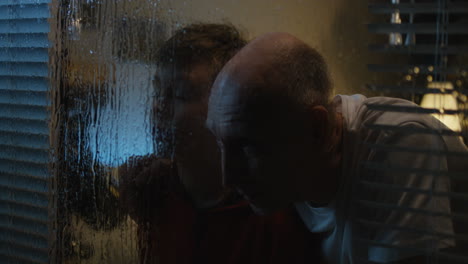 a boy and a man looking through a rainy window at night.