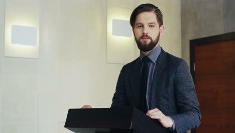 close-up view of caucasian businessman on a podium wearing formal clothes and talking in a conference room, then he looks at the camera and smiles