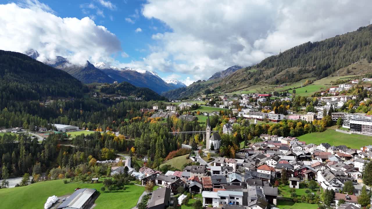 Scuol, switzerland, with green fields, mountains, and scattered buildings, aerial view