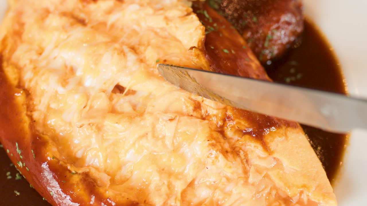 Knife slices fluffy omelette rice, revealing soft interior, in bright restaurant lighting, close-up view