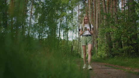 general plan mobile phone in the hands of a female traveler walking through the forest. social networks navigator and messenger. use your mobile phone for a walk in the woods