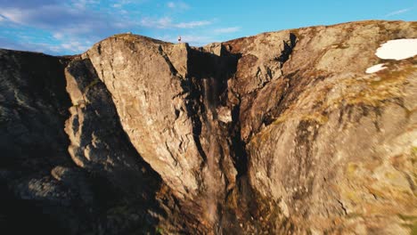 fpv aéreo sobre la cima de la montaña iluminada por el sol en el parque nacional de hardangervidda pasando por un macho encaramado en la cima de un acantilado