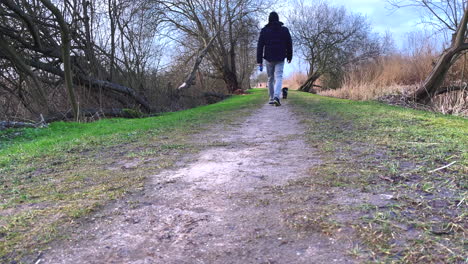 a man walks with his small black bolonka in nature