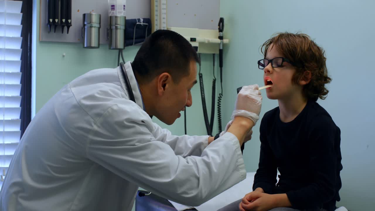 Side view of young asian male doctor examining caucasian boy patient with tool in a clinic 4k