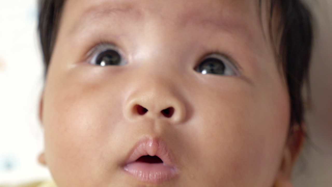 Close-up of a baby girl's sparkling eyes as she practices her developmental skill of rolling over on the bed. Capture this precious milestone in baby growth with a focus on determination and curiosity