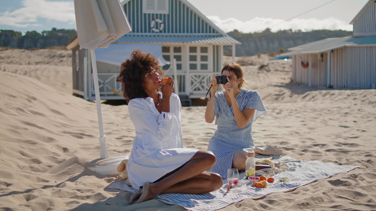 Ragazze gioiose che scattano foto su una spiaggia sabbiosa. Coppia LGBT felice che si gode la vacanza.
