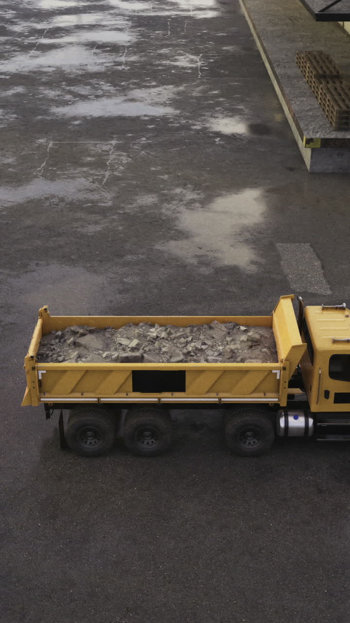 Autocarro con cassone ribaltabile giallo che scarica detriti in una zona industriale nuvolosa