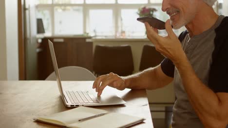 Älterer-Mann,-Der-Mit-Dem-Mobiltelefon-Telefoniert,-Während-Er-Einen-Laptop-4K-Benutzt