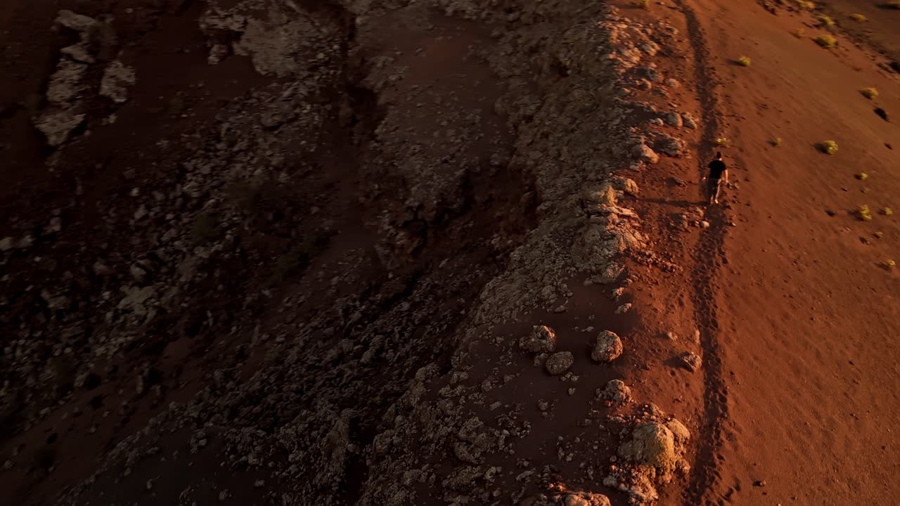 A stunning aerial drone shot capturing a solitary man walking along the rim of Volcano del Cuervo at sunset in Lanzarote, Canary Islands, Spain.