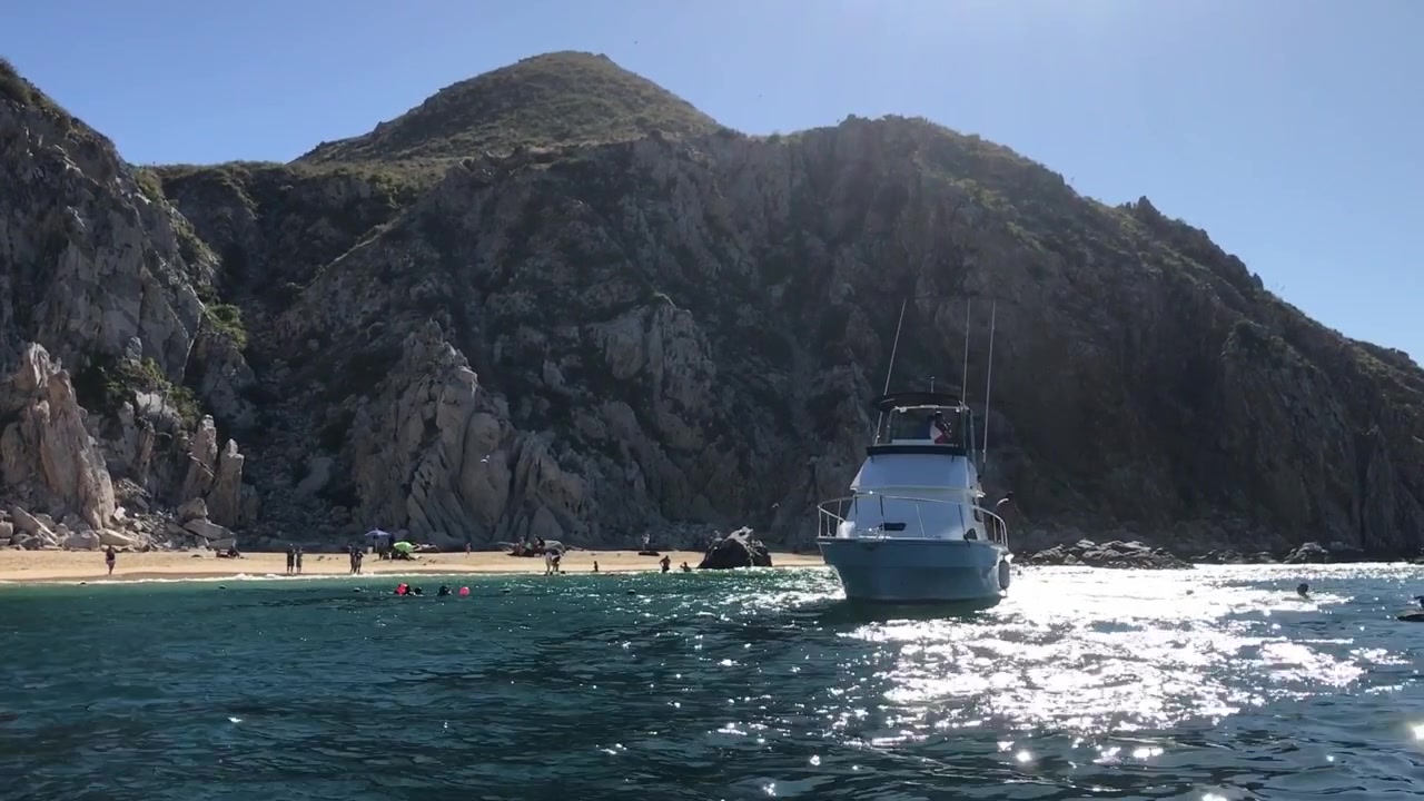 Barca ancorata vicino a una spiaggia rocciosa e a scogliere montuose aspre a Cabo San Lucas, Messico. Acqua cristallina e luce solare intensa creano un paesaggio costiero scenografico per il turismo.
