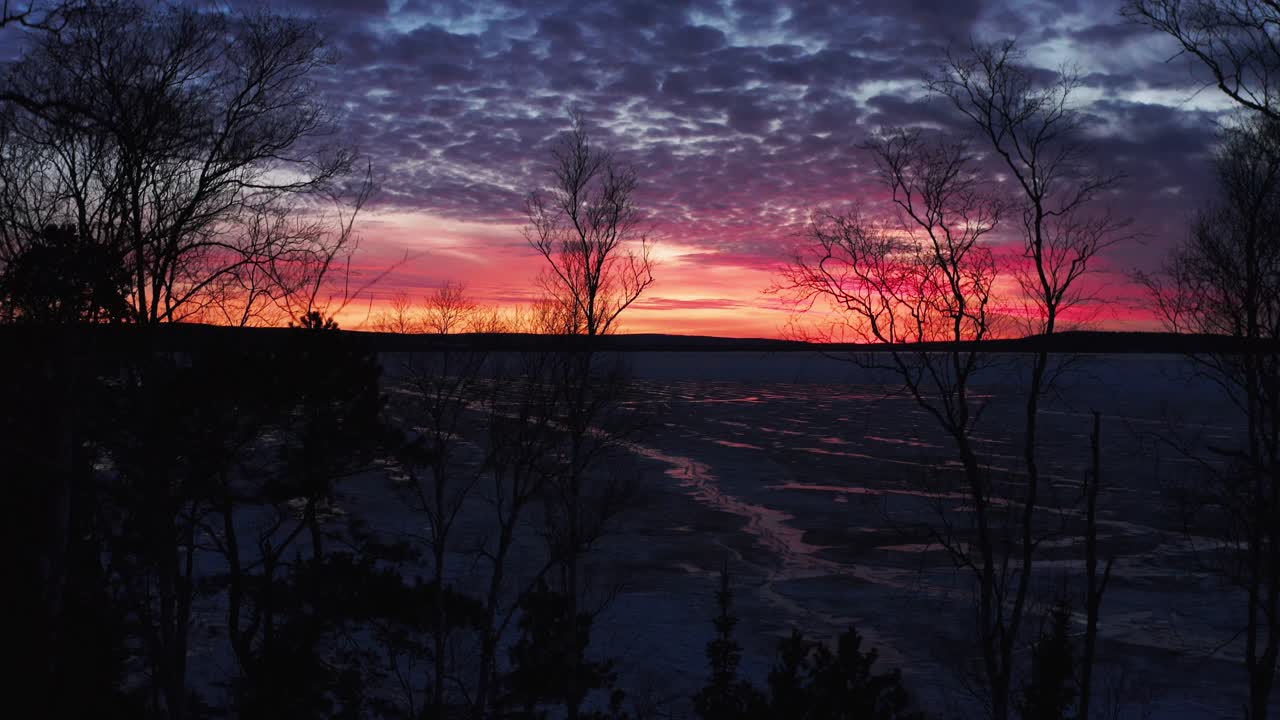 Aerial, dramatic red and orange sunset at dawn at a frozen lake during winter