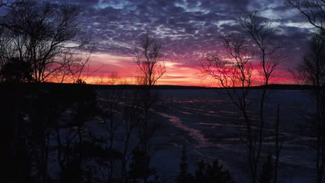 aerial, dramatic red and orange sunset at dawn at a frozen lake during winter