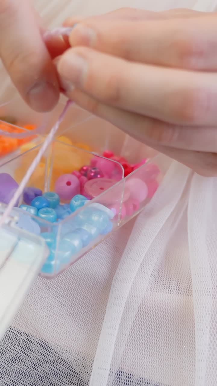 Hands of father and daughter making necklace, close up vertical view