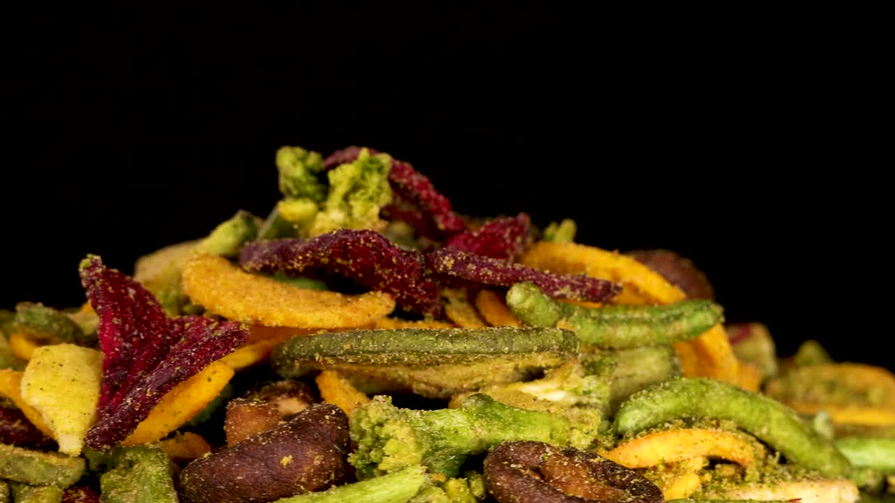 Colorful mixed root vegetable chips rotate on black background, crisp texture highlighted by studio lighting