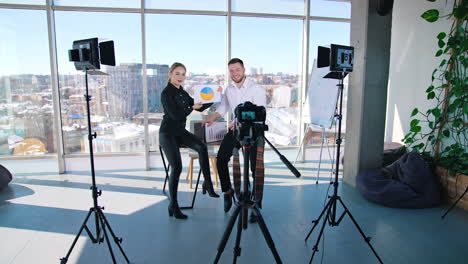 young people speaking on professional camera indoors. beautiful woman showing new blueprint and talking about it on camera. creative young people recording video.
