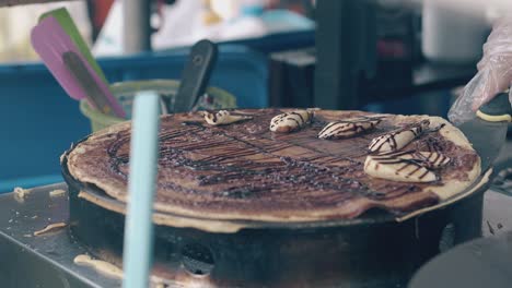 chef-folds-fried-pancake-with-chocolate-and-banana-in-cafe