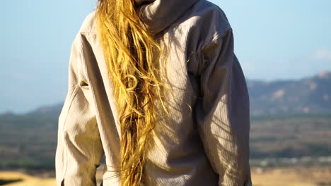 pelo largo y rubio ondulado viento fuerte mujer joven desde atrás de pie en el mirador paisaje natural asombrar vista