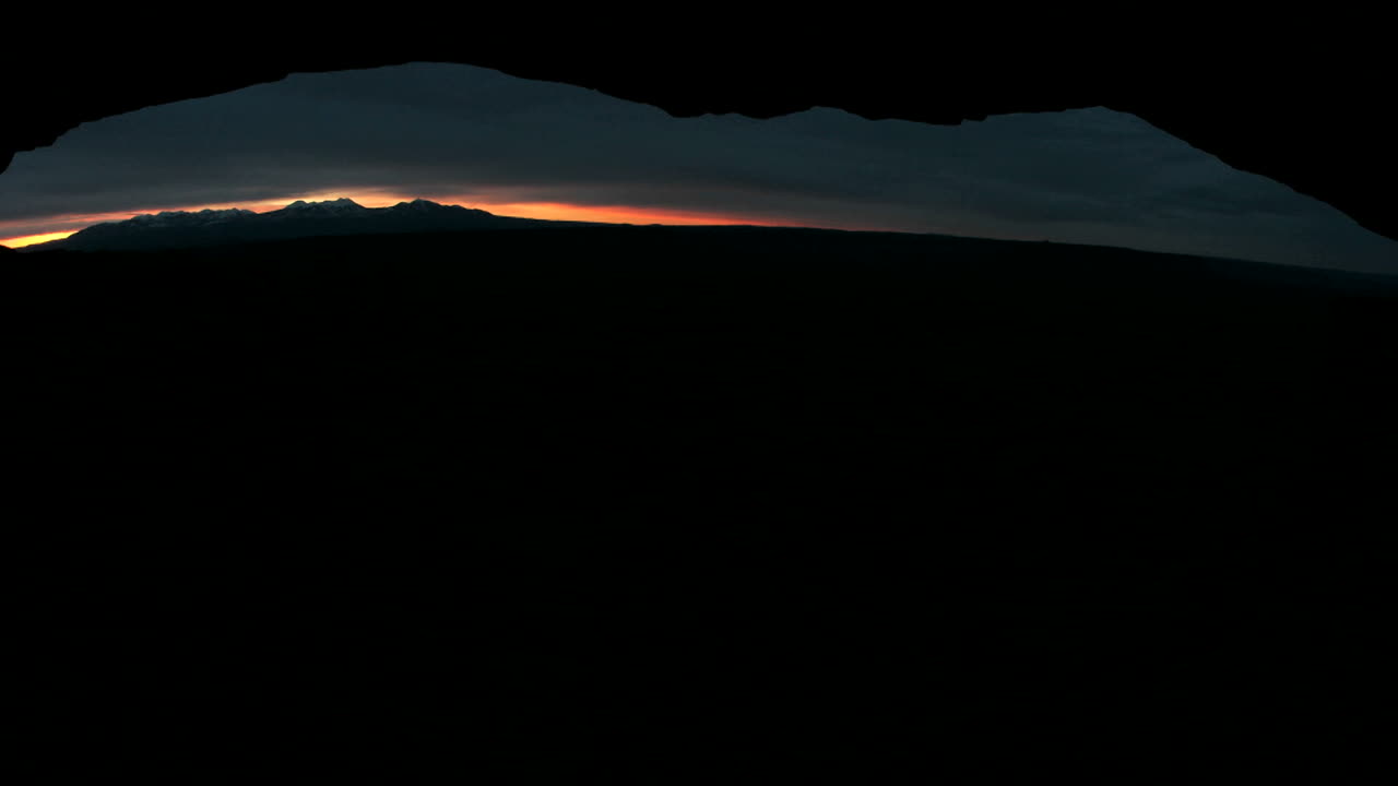 la luz brillante atraviesa el horizonte oscuro durante la hora dorada en el arco de mesa en el parque nacional canyonlands