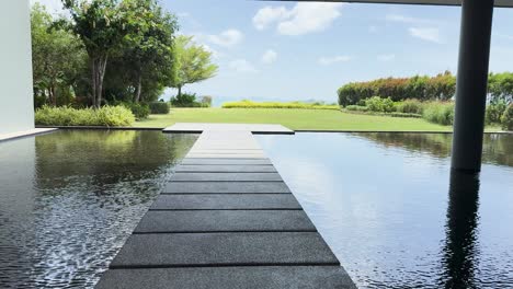 a serene walkway beside a reflective pool at a luxury resort in phuket, thailand, showcasing lush greenery and clear skies