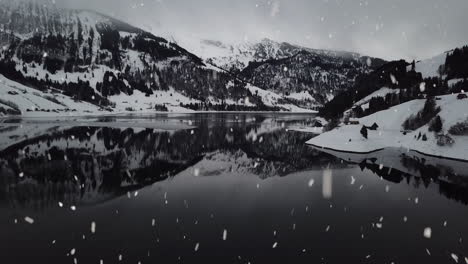 snowy foggy mountain landscape reflects in clear lake water during snowfall, aerial drone tilting up view