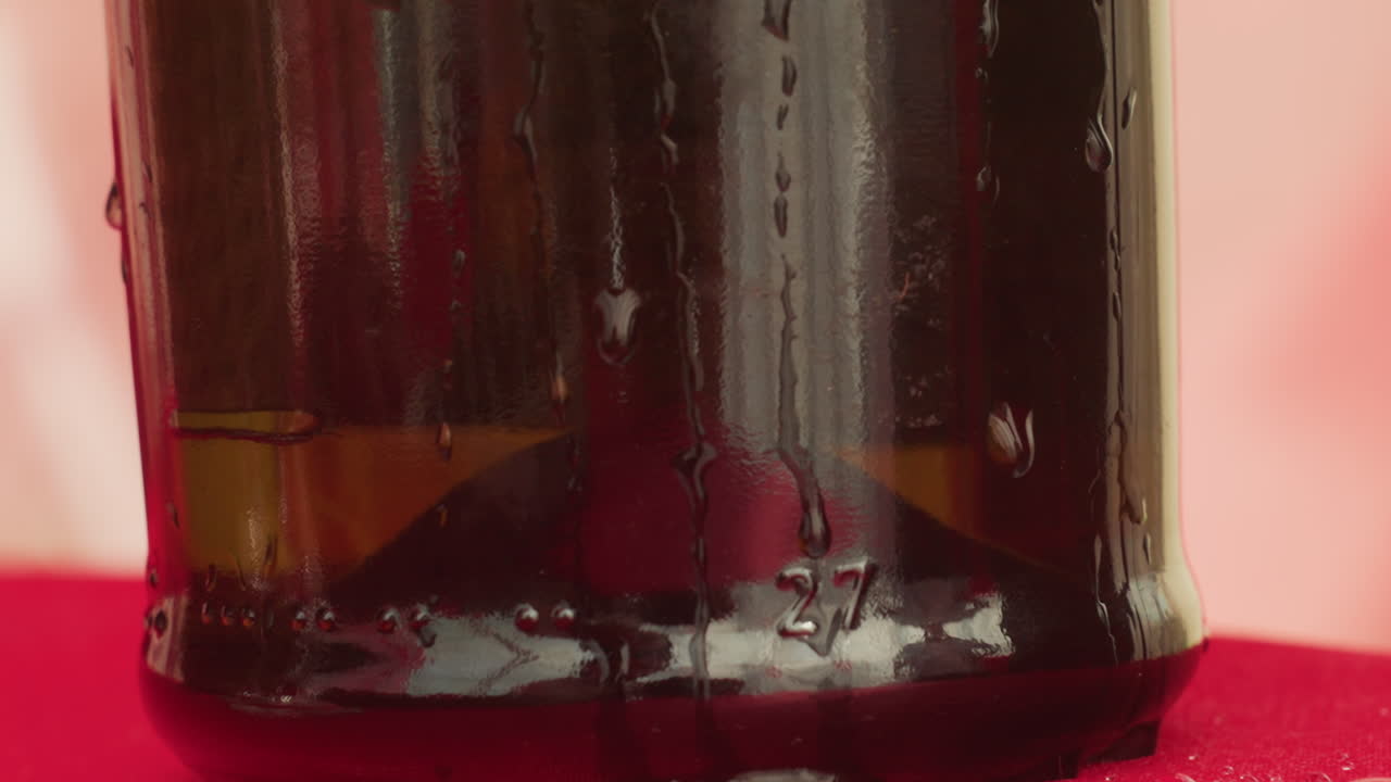 Primo piano della base di una bottiglia di vino su un panno rosso, dettaglio di un appuntamento serale suggestivo con goccioline di condensa, riflesso lucido su vetro scuro, accenno di etichetta vintage, atmosfera accogliente a cena e atmosfera da sommelier
