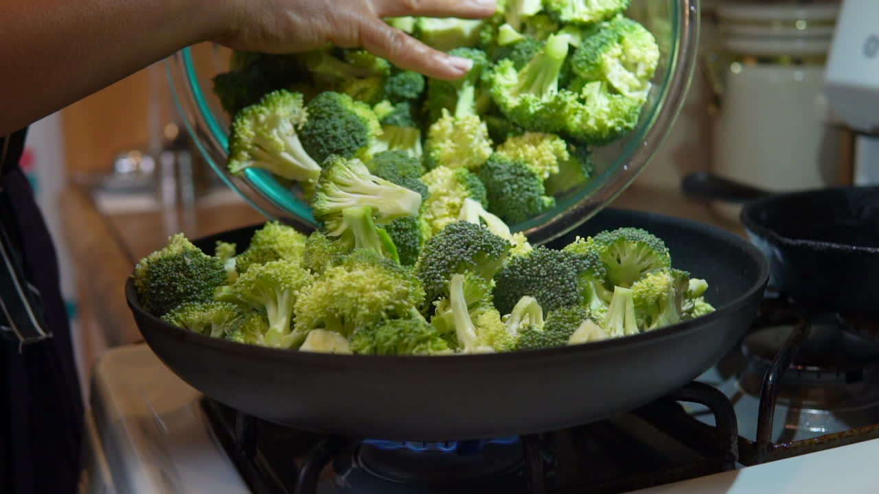 Filling a skillet with freshly cut broccoli to cook, fry or steam - slow motion