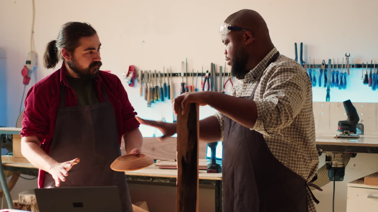 Woodworker looking over blueprints on laptop, brainstorming with colleague
