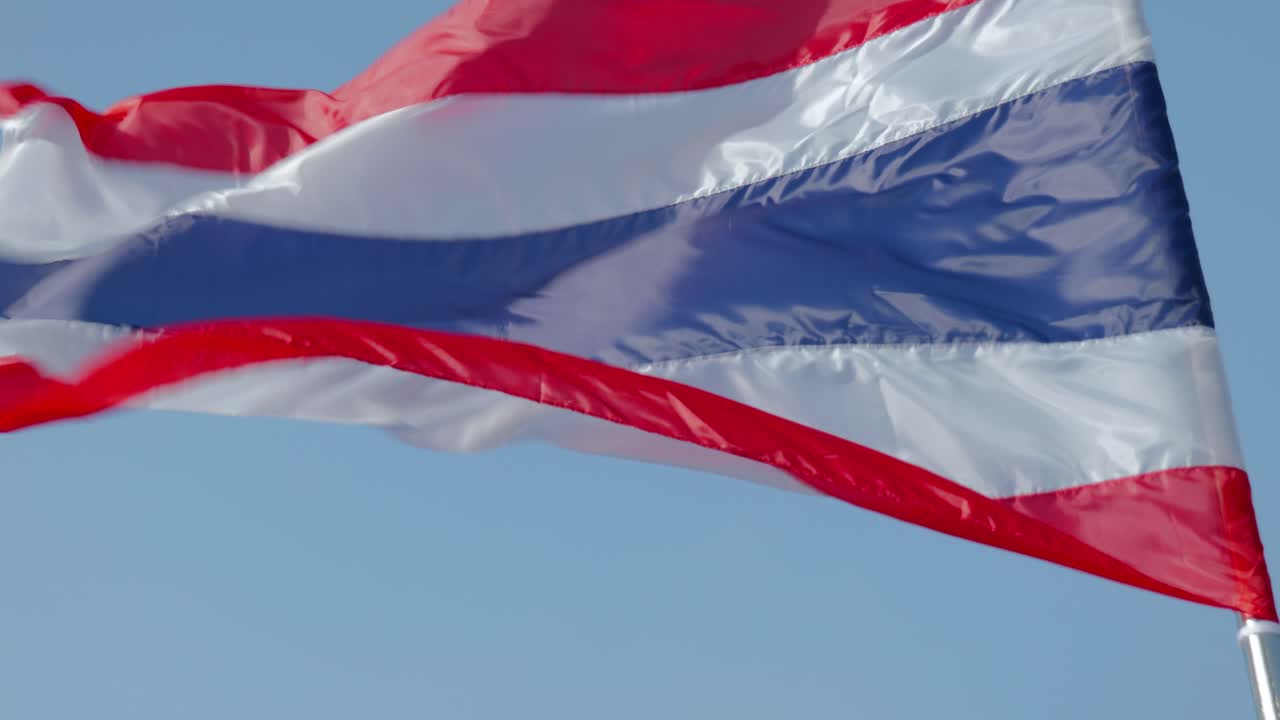 Close-up footage of the national flag of Thailand, known as the Tricolor or Thong Trairong, waving proudly in the wind. Symbol of Thai identity, patriotism, and national pride