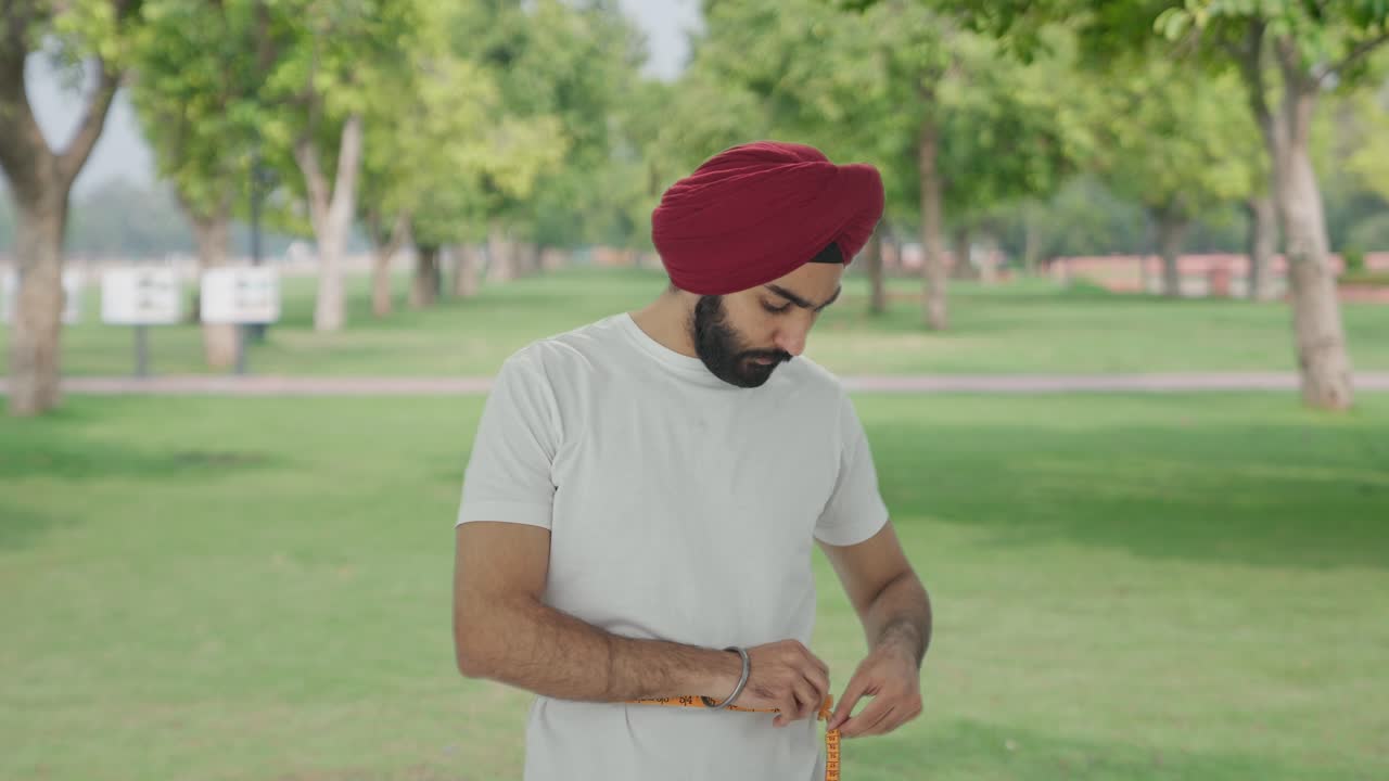 sad sikh hombre indio midiendo la cintura usando cinta de pulgada en el parque