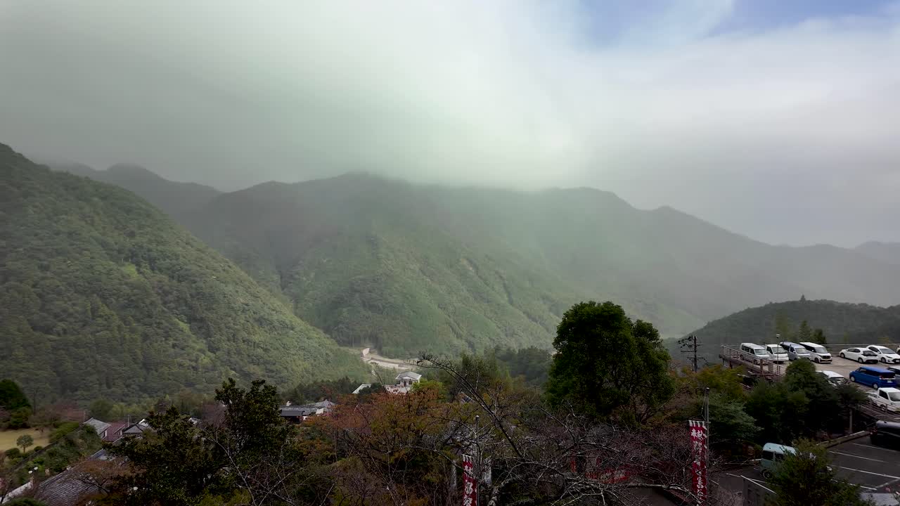 Fog descending on the green slopes of Mount Nachi in Wakayama prefecture, Japan, with a parking lot and some buildings visible in the foreground