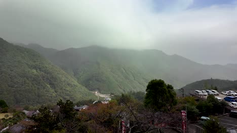 fog descending on the green slopes of mount nachi in wakayama prefecture, japan, with a parking lot and some buildings visible in the foreground