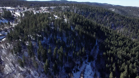 Vista-Aérea-Sobrevolando-Las-Montañas-Nevadas-De-Nuevo-México-Con-Una-Histórica-Armadura-Ferroviaria-De-Vía-Estrecha