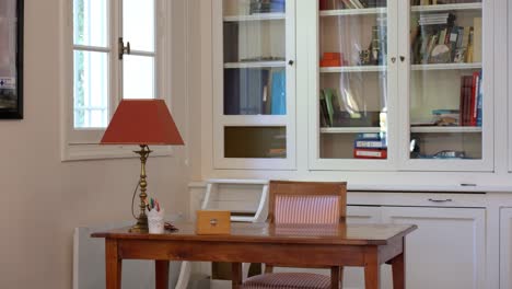 slow establishing shot of a small home office with a glass bookshelf behind