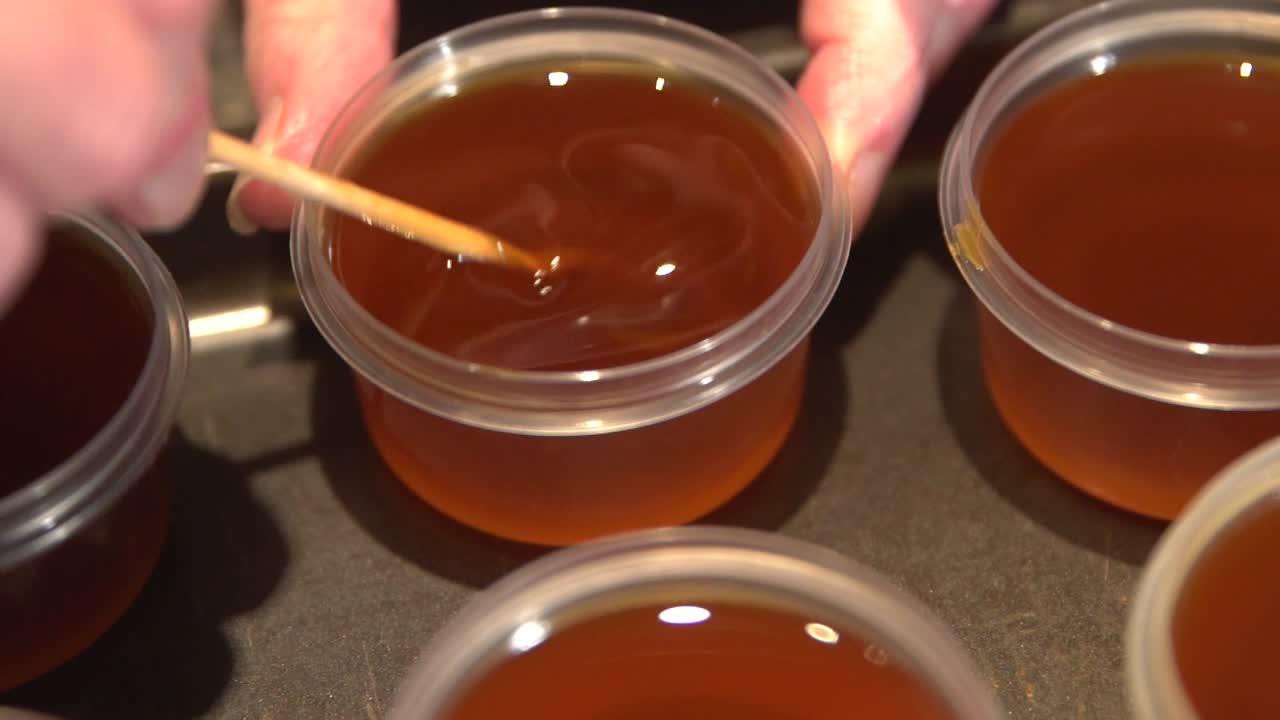 Donna che versa olio essenziale da una bottiglia di vetro in una ciotola sul tavolo.