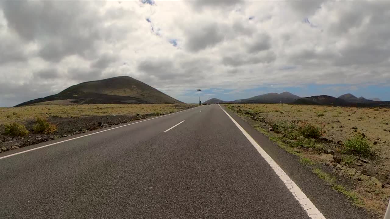 Long distanced road winding through desolate hills under a dramatic sky, Canarias, Lanzarote, Spain.