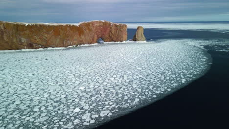 Luftaufnahme-Des-Percé-Felsens-Im-Winter-Mit-Eis-Auf-Dem-Ozean