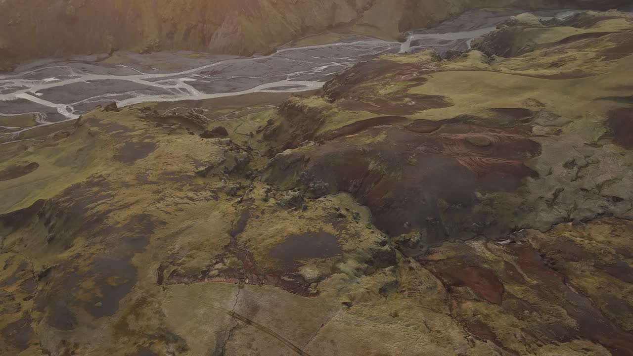 Aerial shot of vibrant volcanic terrain in northern Iceland, with rugged hills and a braided river in the background, showcasing the region’s unique geology.