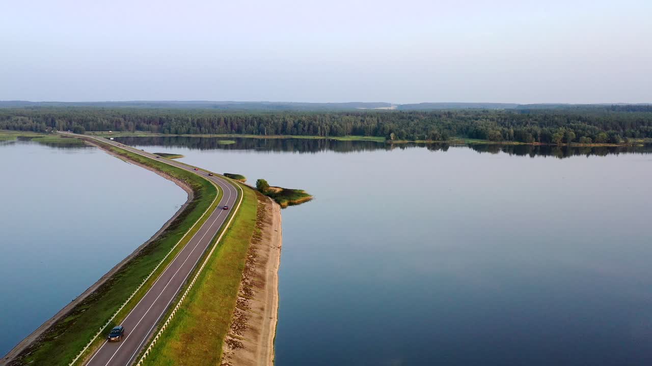 Aerial view of a causeway crossing a large lake with a forest in the background